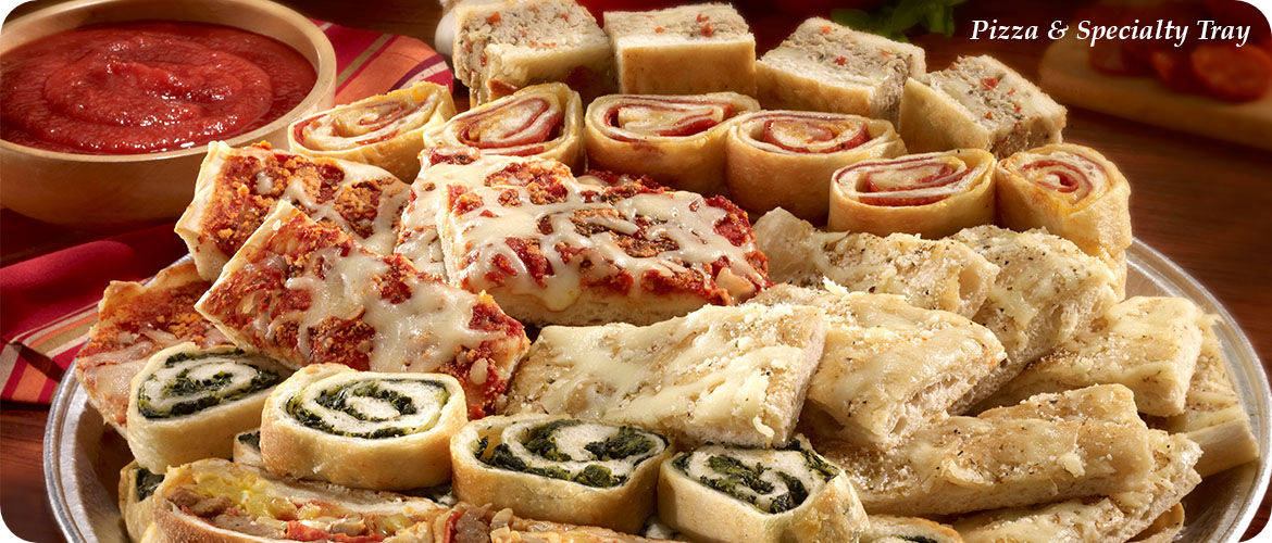 A platter of various sliced pizza and specialty bread rolls with a bowl of marinara sauce in the background.