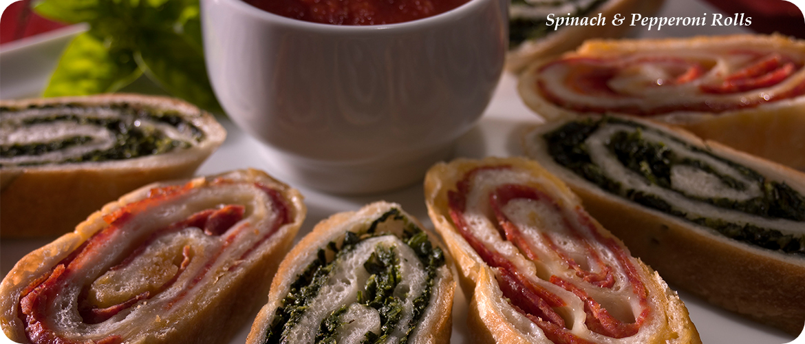 Close-up of sliced spinach and pepperoni rolls arranged around a small bowl of marinara sauce on a white plate.