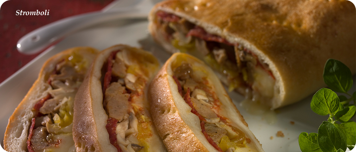 A close-up of a sliced stromboli, revealing its filling of cheese, meats, and vegetables, on a white plate. A sprig of fresh herbs is visible in the foreground.