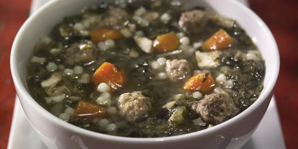 A bowl of soup with meatballs and carrots.