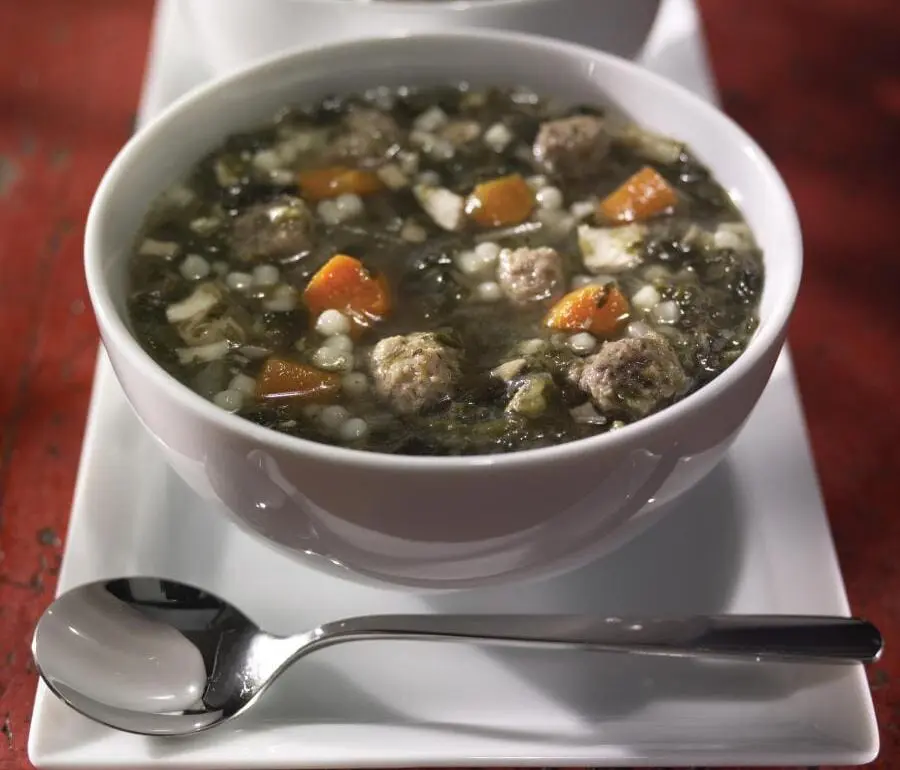 A bowl of soup on a plate with spoon.