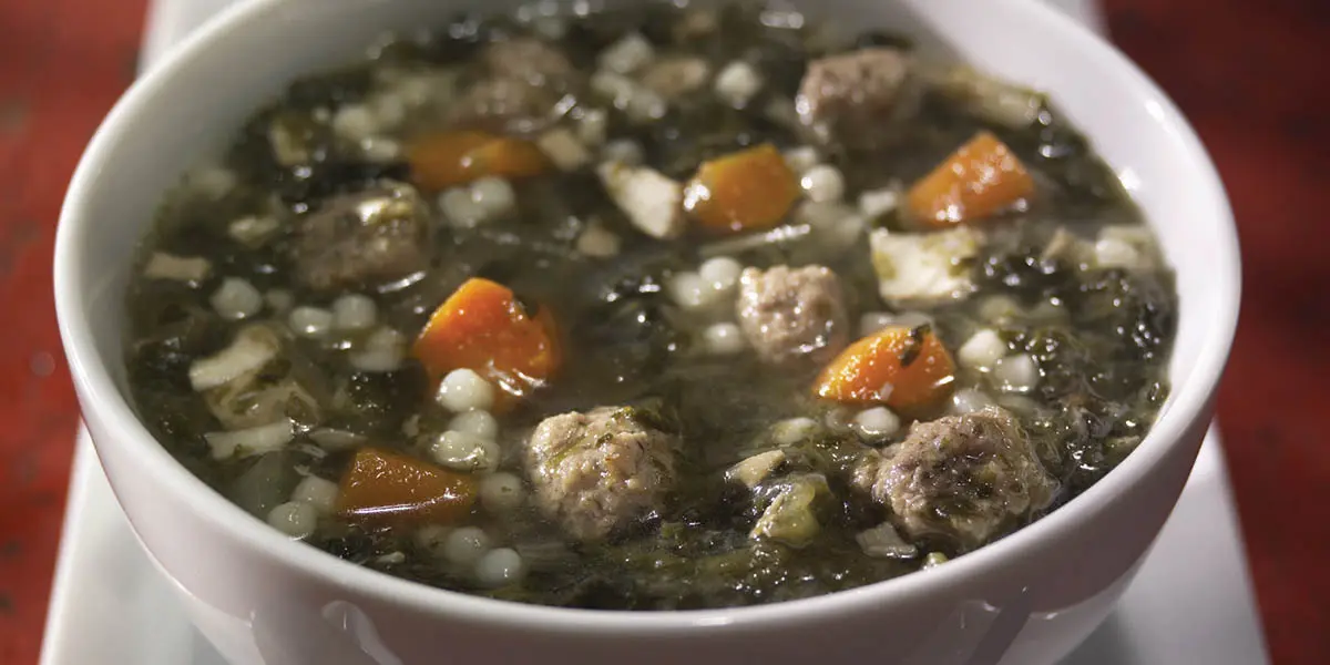 A bowl of soup with meatballs and vegetables.