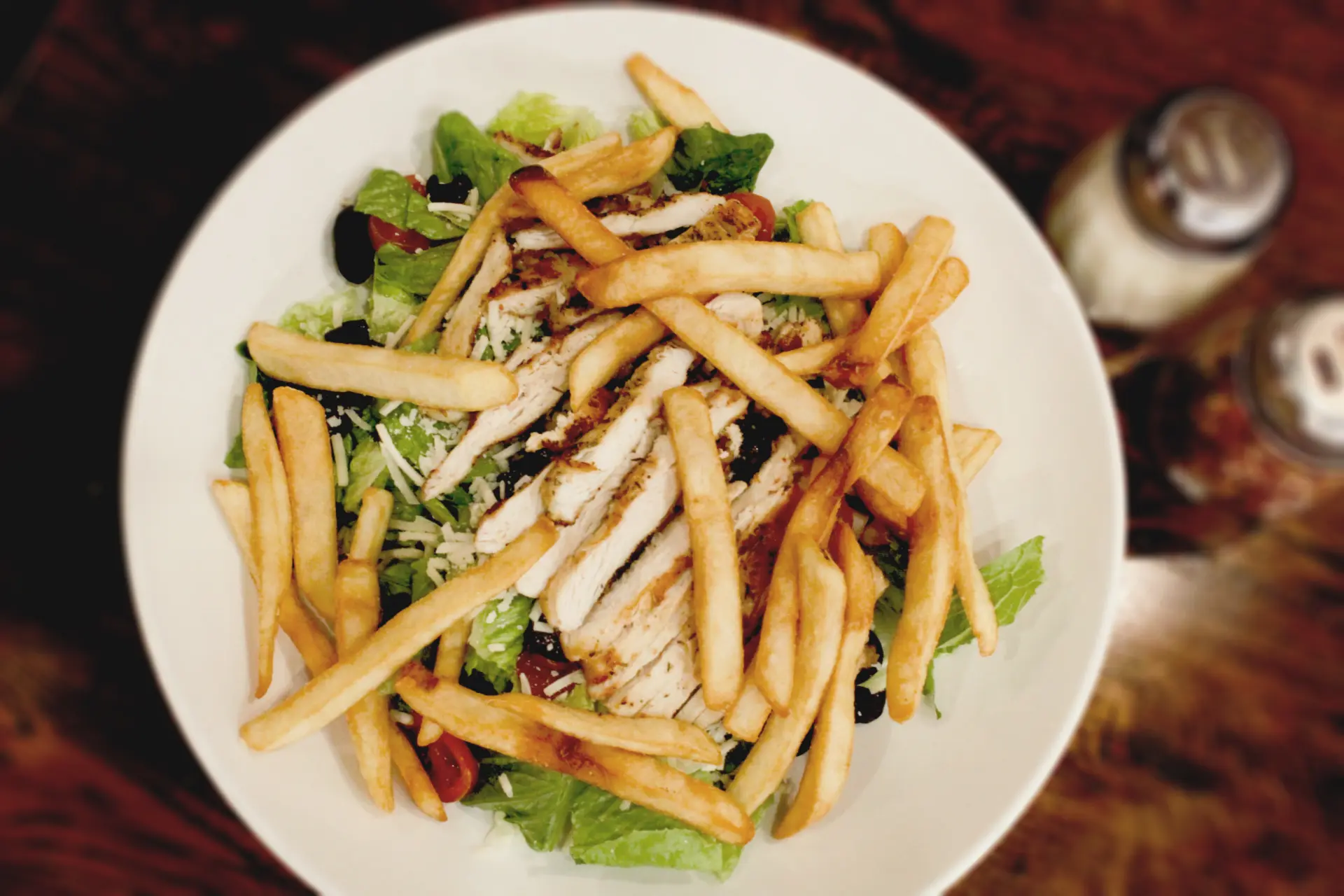 A white bowl filled with salad and french fries.