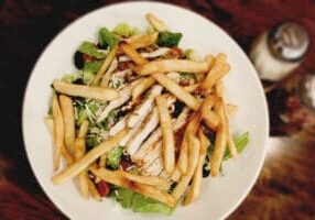 A white bowl filled with salad and french fries.